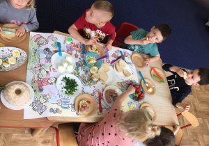 dzieci siedzą przy stolikach z wielkanocnymi potrawami